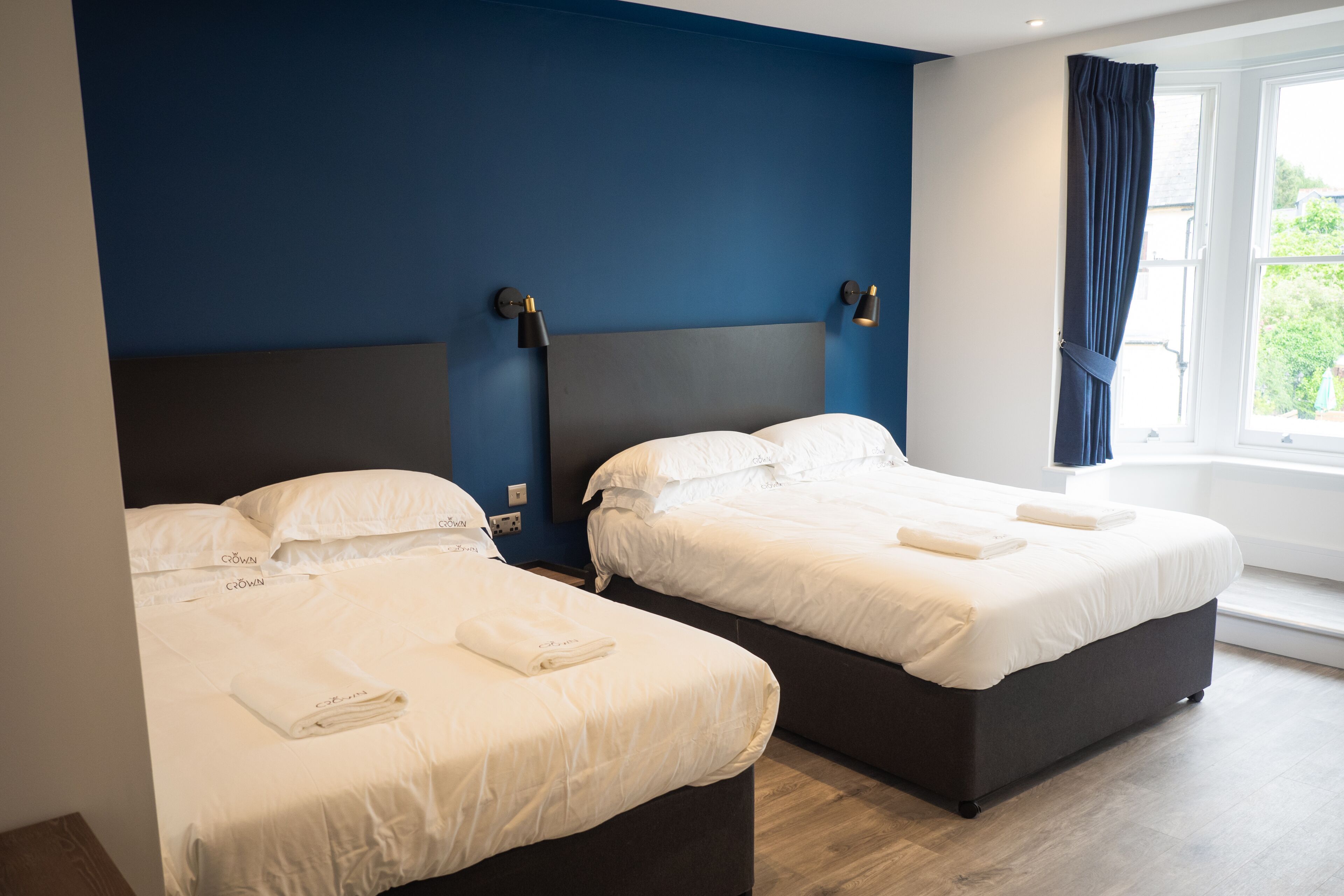 Ett hotellrum med två sängar, en mörk sänggavel och ett fönster med gardiner.