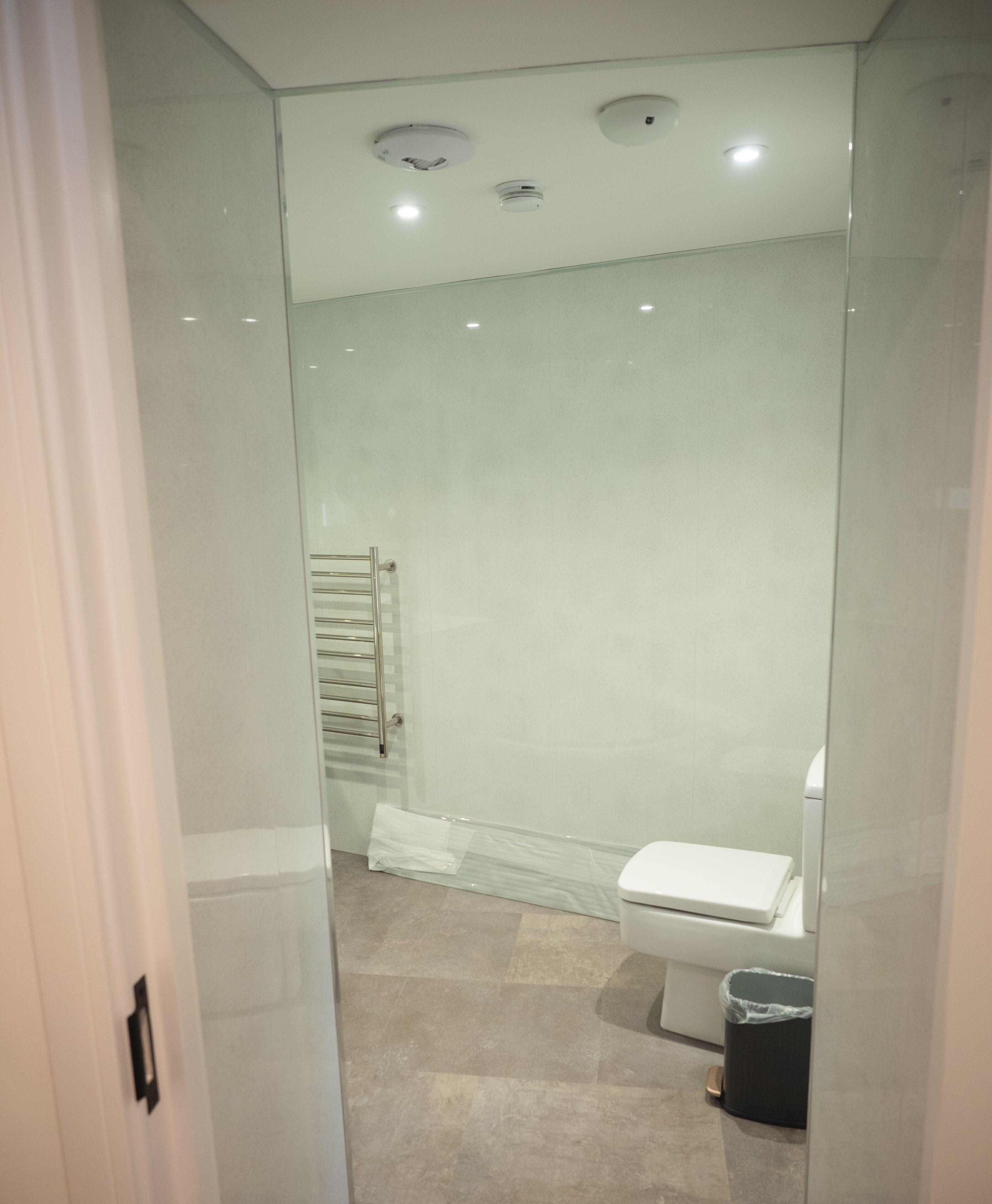 Une salle de bain moderne avec une douche à parois de verre, des toilettes et une poubelle.