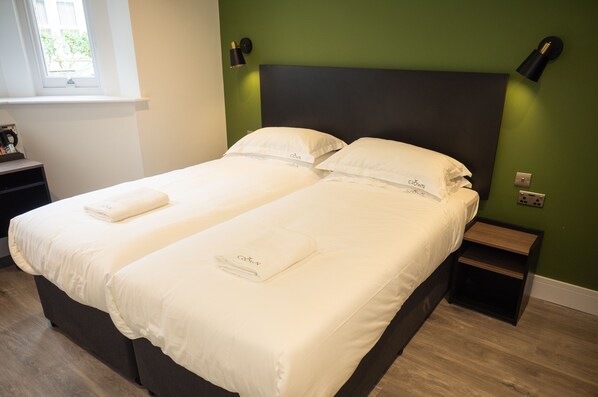 A double bed with white linens and a dark headboard in a room with green walls and two bedside tables. - Crown Hotel (Oxford)