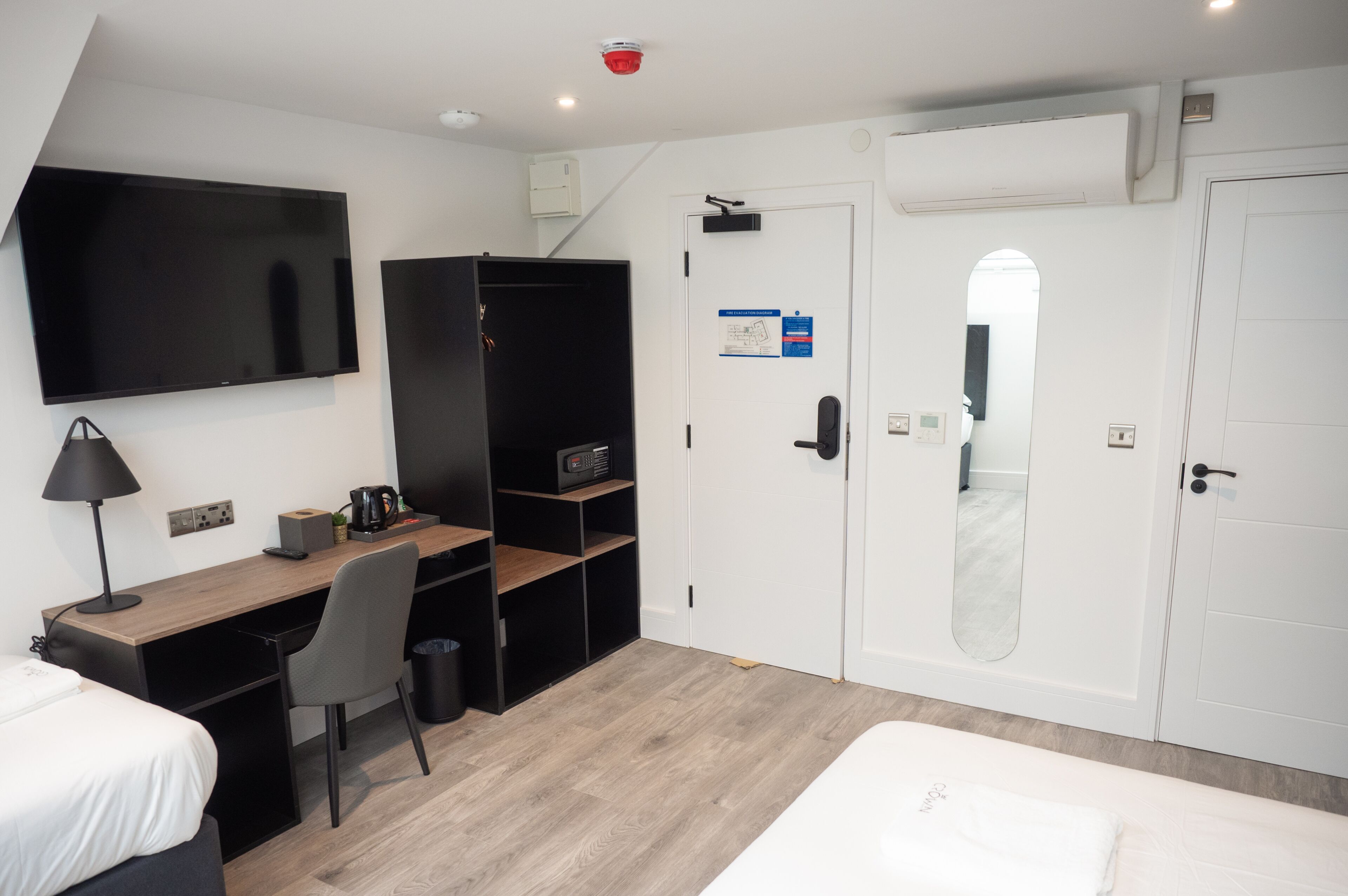 A hotel room with a bed, a desk, a chair, a TV, a wardrobe, and a door with a mirror.