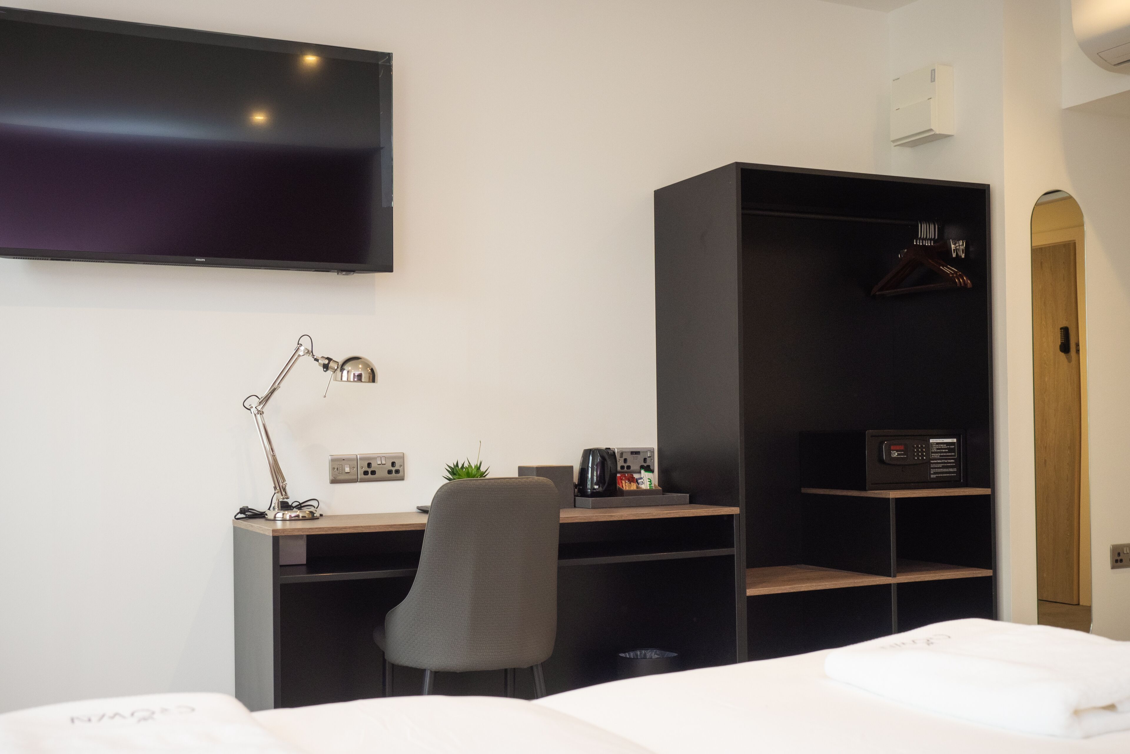 Une chambre d’hôtel comprenant un lit, un bureau avec une chaise, une télévision, un porte-manteau et une armoire.