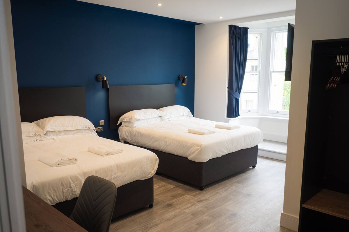 A hotel room with two beds, a desk, and a window with curtains.
