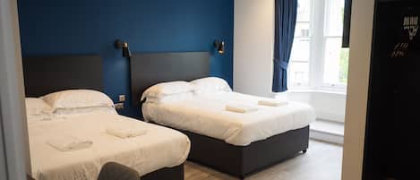 Habitación de hotel con dos camas, un escritorio y una ventana con cortinas.