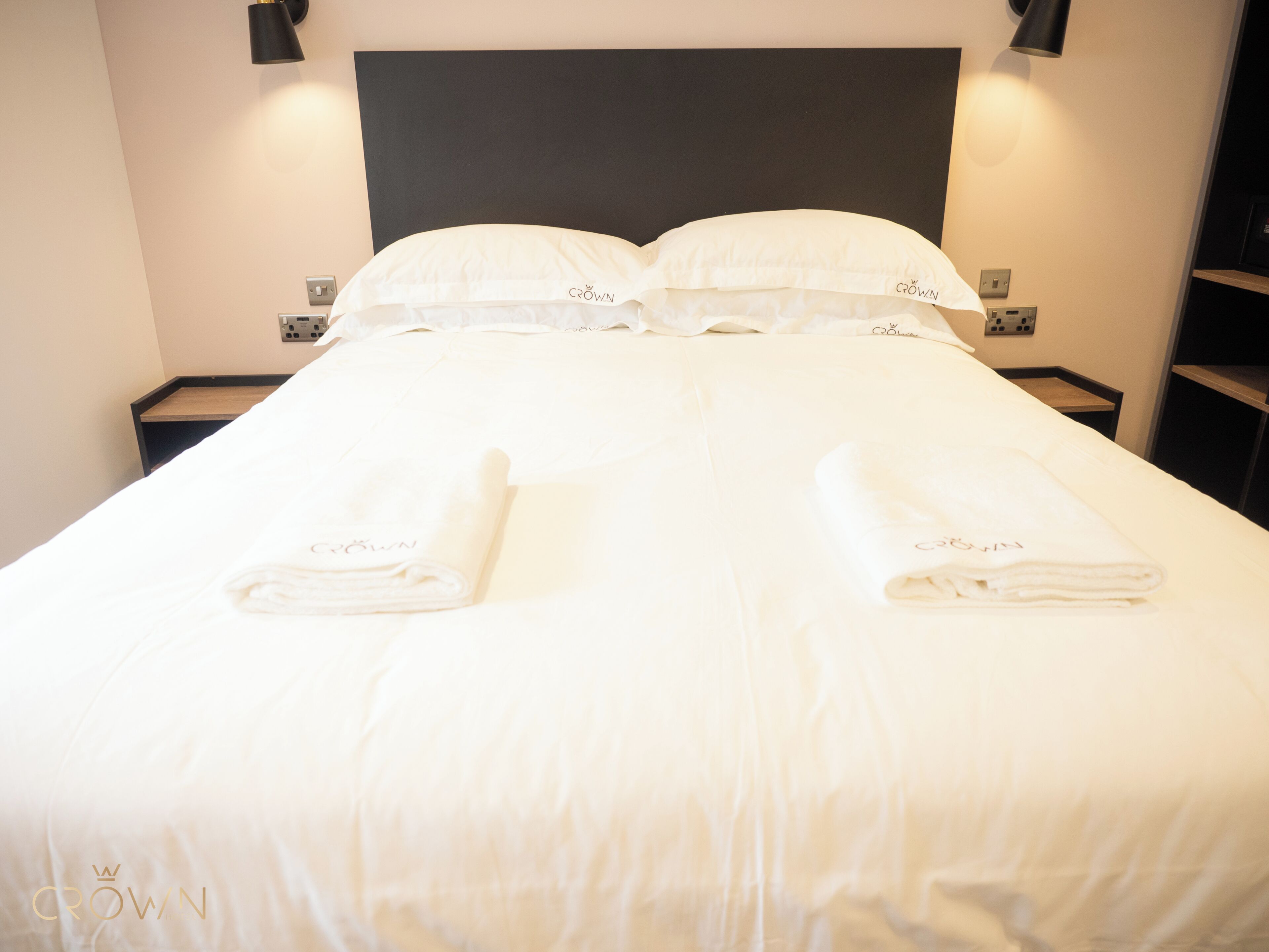 A neatly made bed with white linens and towels, two bedside tables with lamps, and a black headboard.