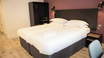 Una cama doble con sábanas blancas, cabecera oscura y una mesita de noche con lámpara.