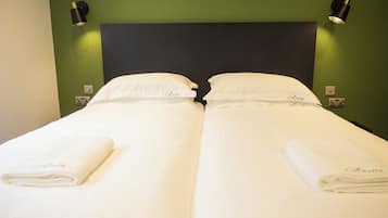 Llits dobles amb roba de llit i coixins blancs, dues taules de nit amb làmpades i una paret verda.