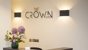 A reception desk with a modern design, a sign above it reading "CROWN HOTEL", and a vase with flowers on the left side. - Crown Hotel (Oxford)