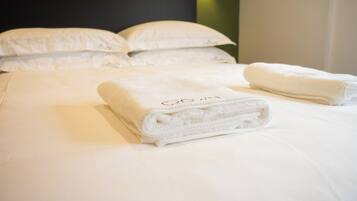 A neatly made bed with white linens and pillows, a folded towel on the bed, and a logo 'CROWN' on the headboard.
