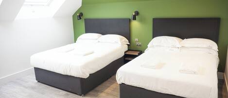 Habitación de hotel con dos camas, tragaluz, pared de acento verde y piso de madera.
