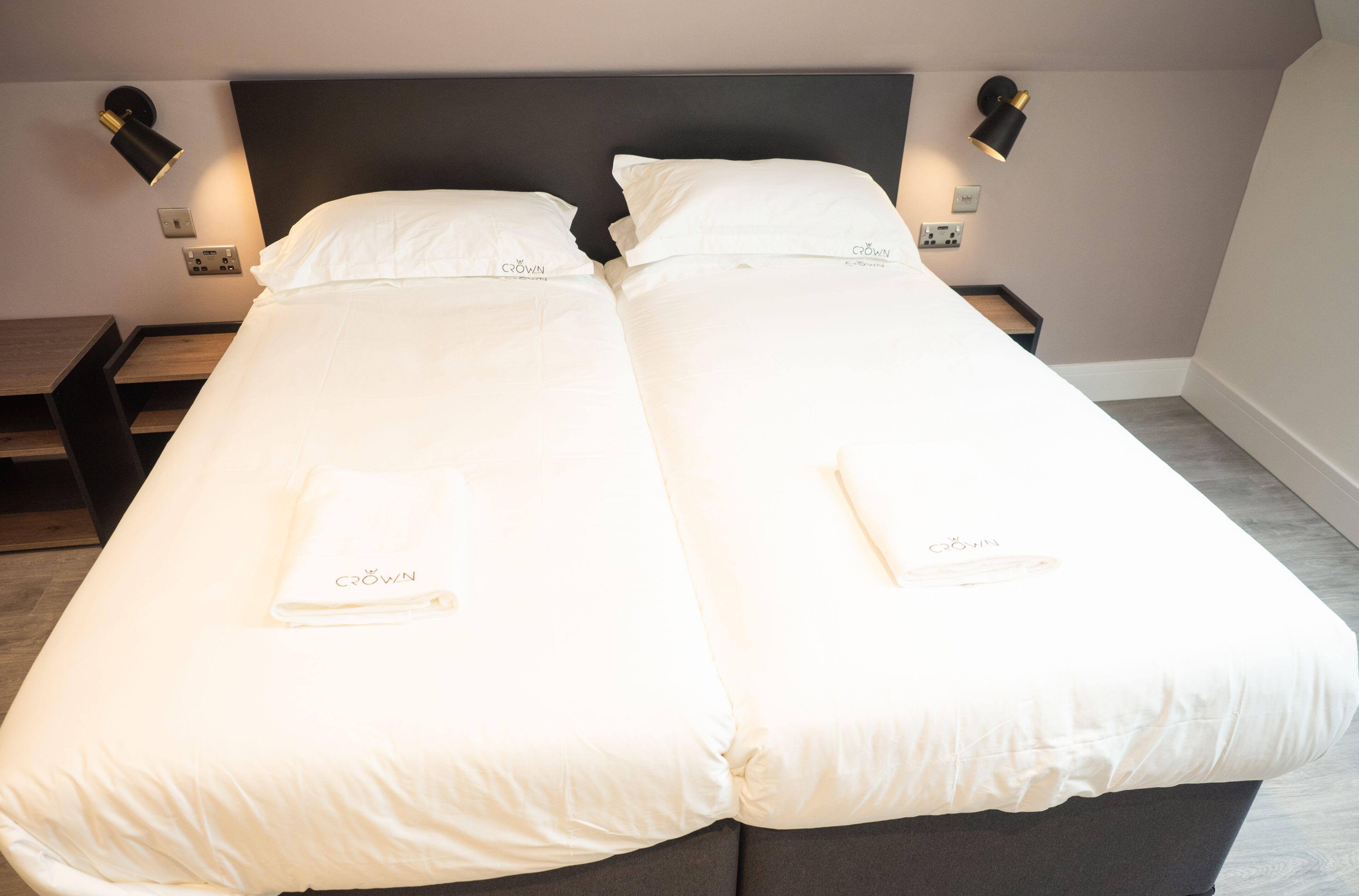 A double bed with white linens and a matching pillow, two bedside tables, and wall-mounted reading lamps.