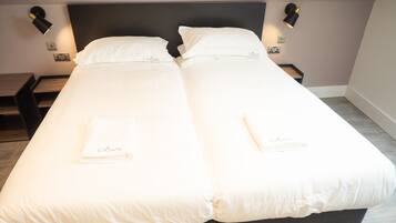 A double bed with white linens and a matching pillow, two bedside tables, and wall-mounted reading lamps.