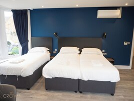 Quarto de hotel com duas camas, paredes azul-escuro e uma janela com cortinas.