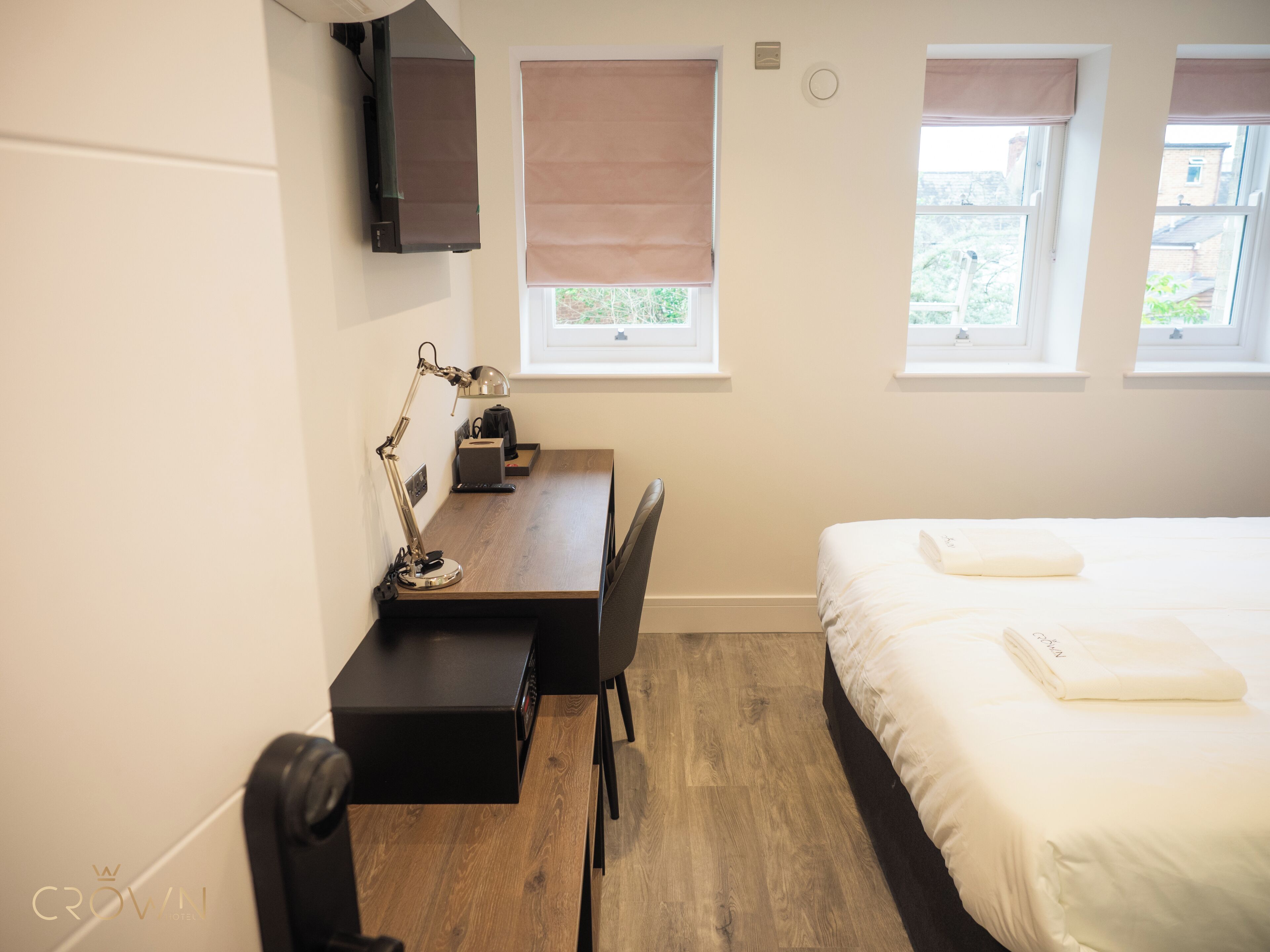 A hotel room with a bed, a desk with a lamp, a chair, and a TV on the wall.