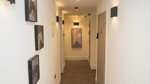 A hotel hallway with framed artwork on the walls, a carpeted floor, and a wooden door at the end. - Crown Hotel (Oxford)