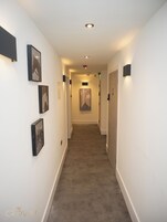 A hotel hallway with framed artwork on the walls, a carpeted floor, and a wooden door at the end.