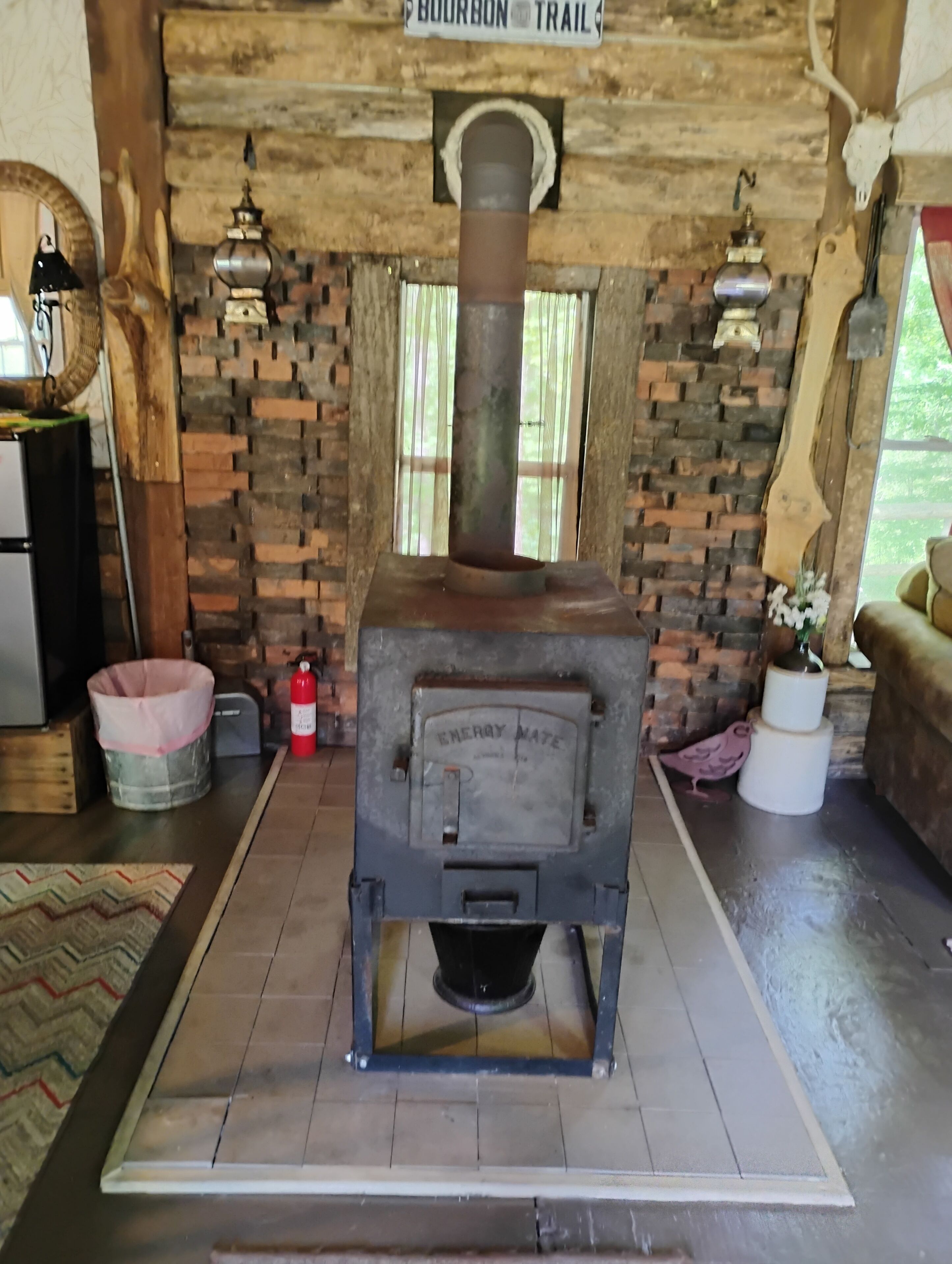 A wood-burning stove in a rustic room with a brick wall, a sign above it, and a window.