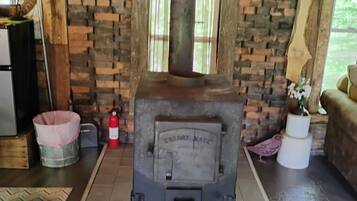 A wood-burning stove in a rustic room with a brick wall, a sign above it, and a window.