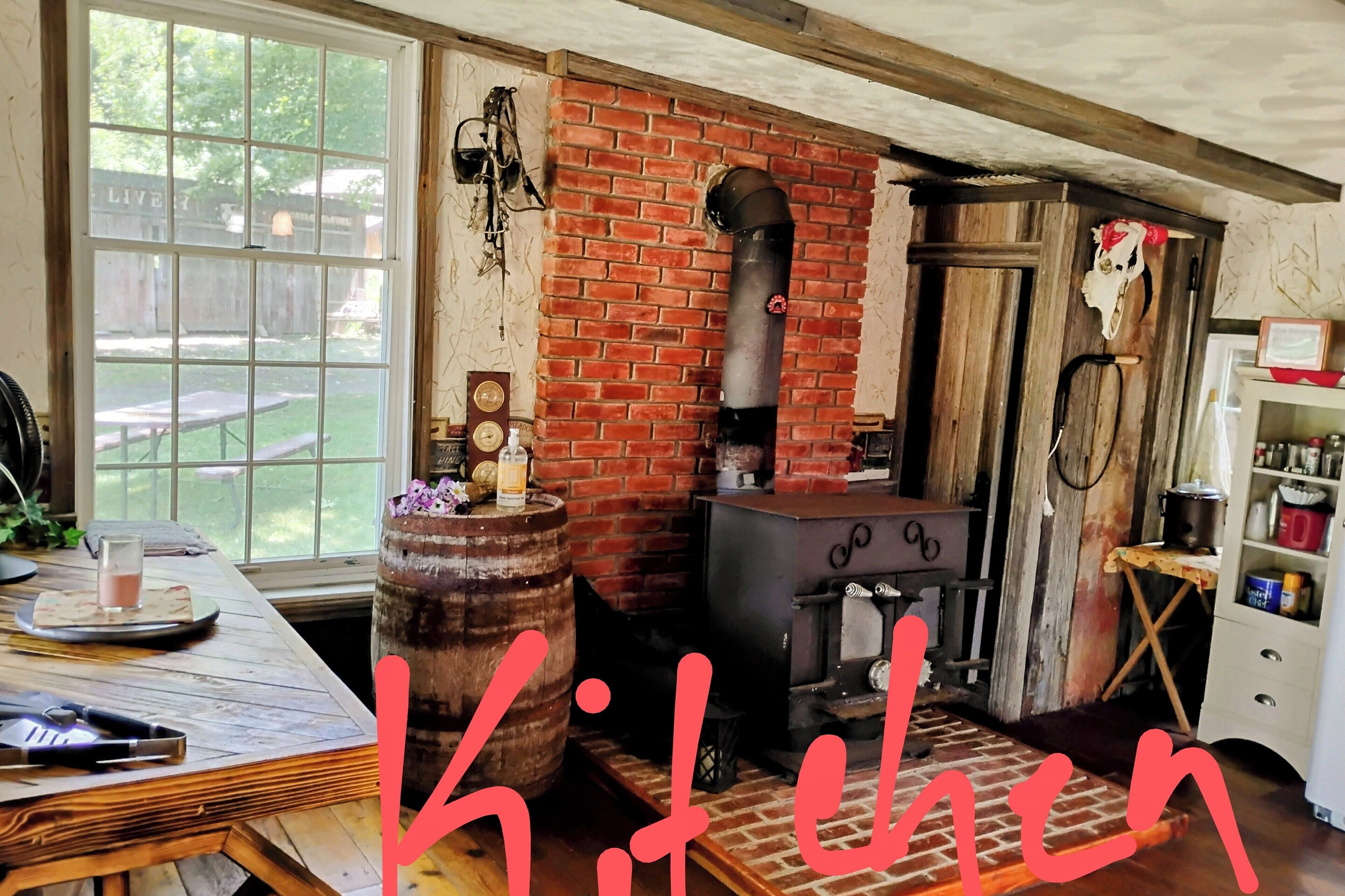A rustic kitchen with a brick wall, a wood-burning stove, and a wooden table with a glass of milk.