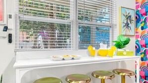Una cocina con encimera blanca, cuatro taburetes dorados, una ventana con persianas y una pared colorida.