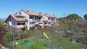 Un edificio residencial de varios pisos con un jardín cuidado y una zona de juegos.
