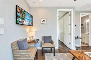 Ein Wohnzimmer mit einer Couch, einem Sessel und einem Couchtisch. An der Wand hängt ein Gemälde und auf einem Beistelltisch steht eine Lampe.