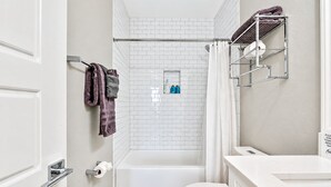 Un baño con una bañera blanca, un inodoro, una ducha con cortina y un perchero con toallas.