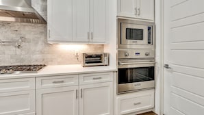 Una cocina con armarios blancos, microondas integrado, horno tostador y estufa.