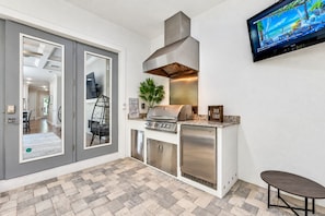 Une cuisine moderne dotée d’un barbecue intégré, d’un téléviseur à écran plat et d’un coin repas avec une chaise.