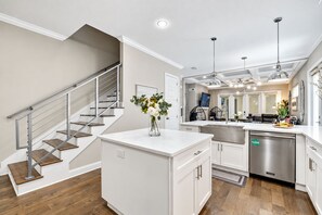 Une cuisine moderne dotée d’un îlot central, d’appareils électroménagers en acier inoxydable et d’un escalier avec une rampe en verre.