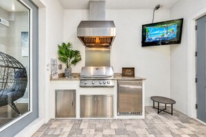 Une cuisine moderne équipée d’une cuisinière en acier inoxydable, d’un barbecue intégré et d’un téléviseur à écran plat fixé au mur.