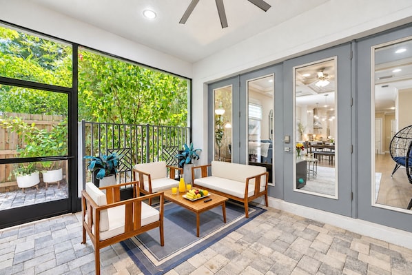 A spacious patio with a wooden table, chairs, and a view of lush greenery through large windows.