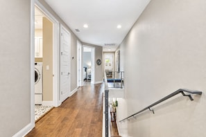 A hallway with a wooden floor leading to a bedroom with a bed and a nightstand.