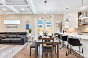Eine moderne Küche mit Essbereich, ausgestattet mit einem schwarzen Ledersofa, einem Esstisch mit Stühlen, Pendelleuchten und Blick ins Freie.