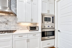 A kitchen with white cabinetry, a stainless steel range hood, a built-in oven, and a toaster oven. - Discover A+ Luxury Living: Brand New Home in Prime Tampa Location! (Tampa)