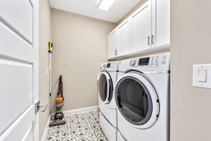 A laundry room with two front-loading washing machines, a vacuum cleaner, and a door.