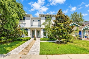 A modern two-story house with a paved driveway leading to a front door, surrounded by well-maintained lawns and trees.