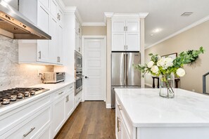 A modern kitchen with white cabinetry, stainless steel appliances, a marble countertop, and a wooden floor.