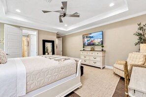 Ein Schlafzimmer mit einem Bett, einer Kommode, einem Sessel, einem Deckenventilator und einem Fernseher an der Wand.