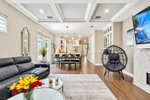 A modern living room with a black leather sofa, a glass coffee table with flowers, a dining area with a white table and chairs, and a black egg chair.