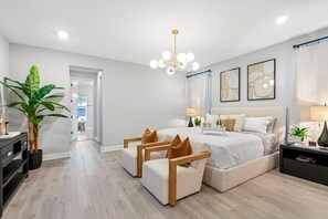 Un dormitori modern amb llit, taules de nit, una planta i un penjador.