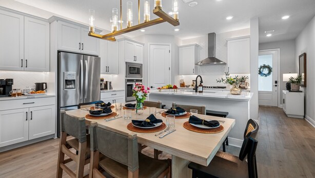 A modern kitchen with white cabinetry, stainless steel appliances, and a wooden dining table set for four.