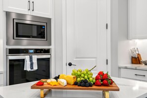 Una cocina con una tabla de madera que muestra varios quesos, uvas, fresas y frambuesas.
