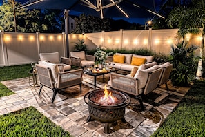 Eine Außenpatio-Terrasse mit Feuerstelle, Sitzgelegenheiten und Lichterketten.