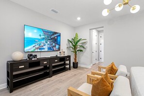 Una sala de estar moderna con un televisor de pantalla plana grande, un mueble de entretenimiento de madera oscura, una planta en maceta y un área de descanso con cojines.