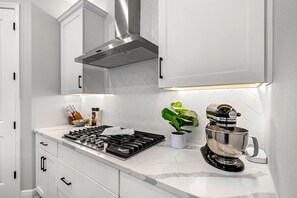 Cuina moderna amb armaris blancs, campana extractora d'acer inoxidable, fogó a gas, cafetera i una planta en test.