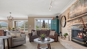 A cozy living room with a fireplace, comfortable seating, and a view of the outdoors. - Mountain Manor | Lake Views & Access | Fenced Yard (Invermere)