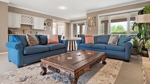 A living room with two blue sofas, a wooden coffee table, and a large window with a view of greenery. - Mountain Manor | Lake Views & Access | Fenced Yard (Invermere)