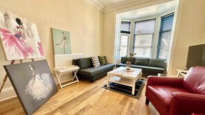 Un salon avec un canap é gris, un fauteuil rouge, une table basse et un tableau accroché au mur.