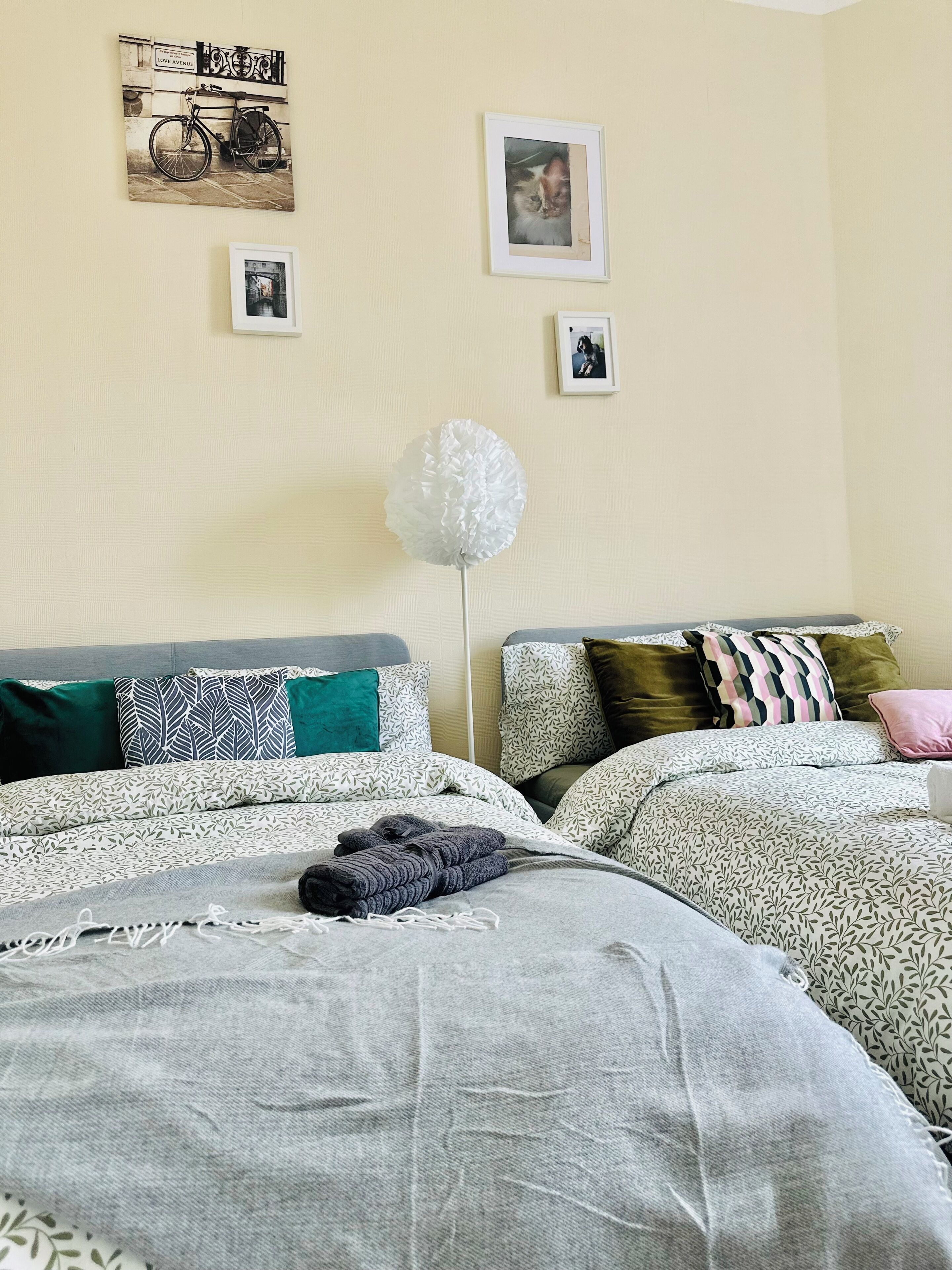 Quarto com duas camas, roupa de cama estampada, uma esfera decorativa branca e quadros nas paredes.