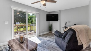 Un salon moderne doté d’un ventilateur de plafond, d’un téléviseur à écran plat, d’un canapé en cuir foncé et d’une porte-fenêtre coulissante donnant sur une terrasse.